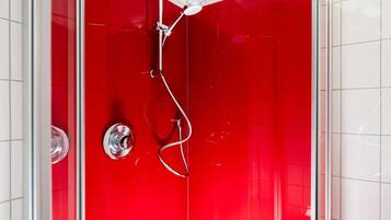 A red-tiled shower enclosure with a handheld showerhead and a wall-mounted faucet.