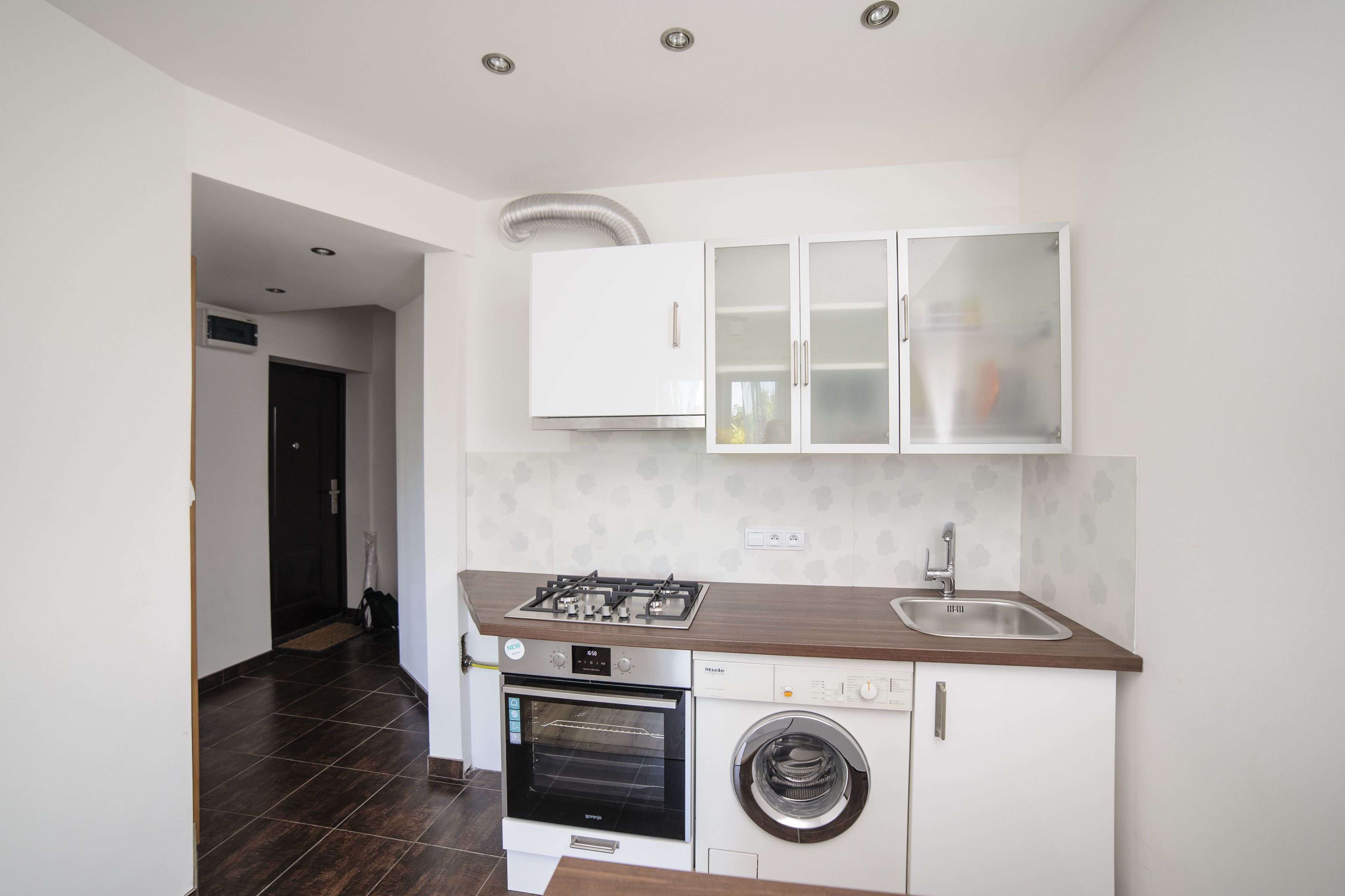 A modern kitchen with a built-in oven, a washing machine, and a stainless steel sink.