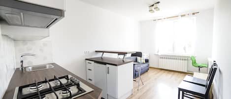 A compact kitchen with a gas stove, a sink, and a compact refrigerator. There is a dining area with a table and chairs, and a window providing natural light.
