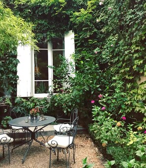 Un patio jardín con mesa y sillas, rodeado de follaje exuberante y plantas con flores.