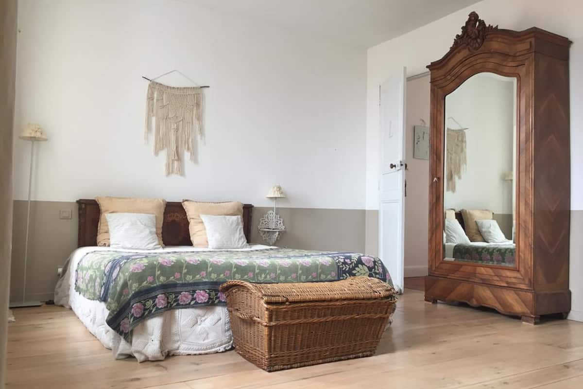 Quarto com cama, espelho, cesta de vime e um objeto decorativo na parede.