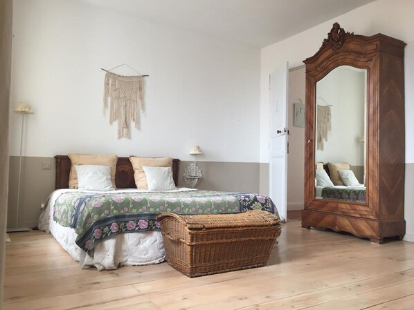 Un dormitorio con una cama, un espejo, una cesta de mimbre y un adorno de pared.