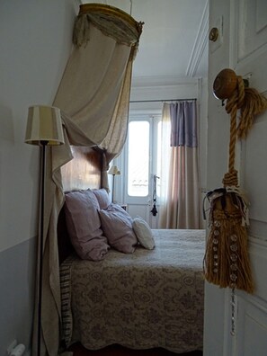 Un dormitorio con cama a dosel, una lámpara de noche, una ventana con cortinas y una cuerda decorativa en la pared.