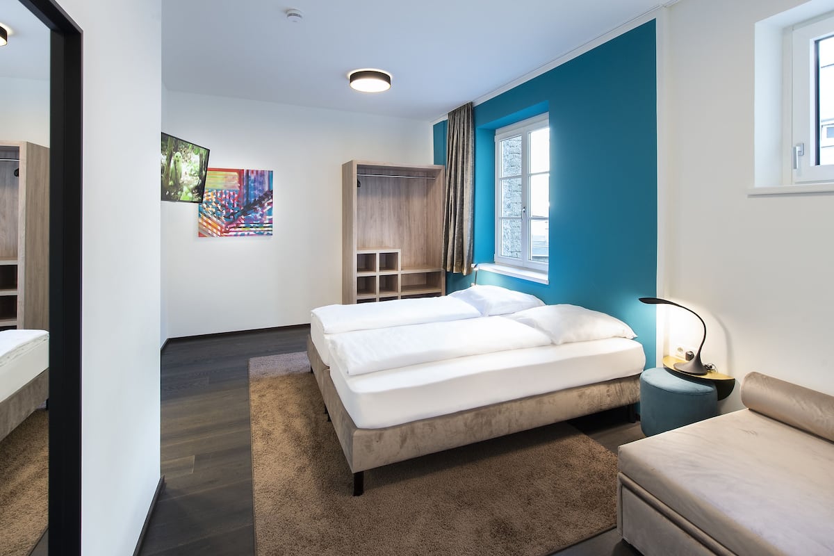 A modern bedroom with a bed, a wardrobe, a desk, and a window.