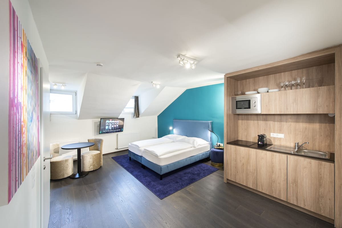 A modern bedroom with a bed, a desk, and a kitchenette.