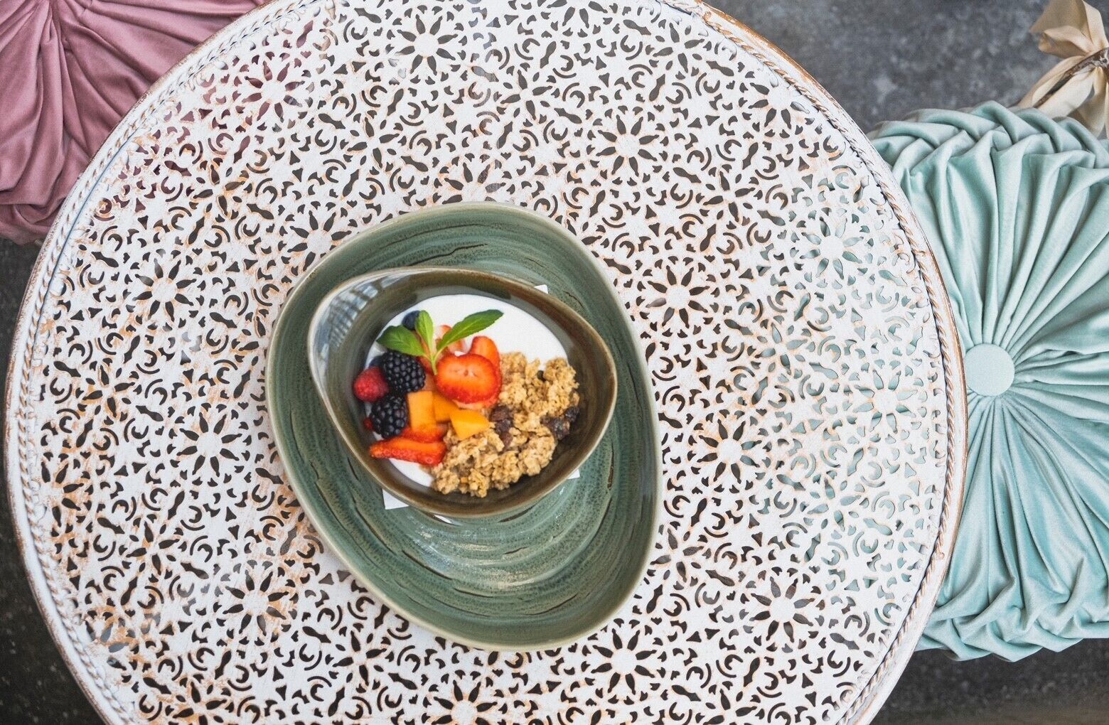 Ein runder Tisch mit einer grünen Schüssel, gefüllt mit einer Mischung aus Früchten und Granola.