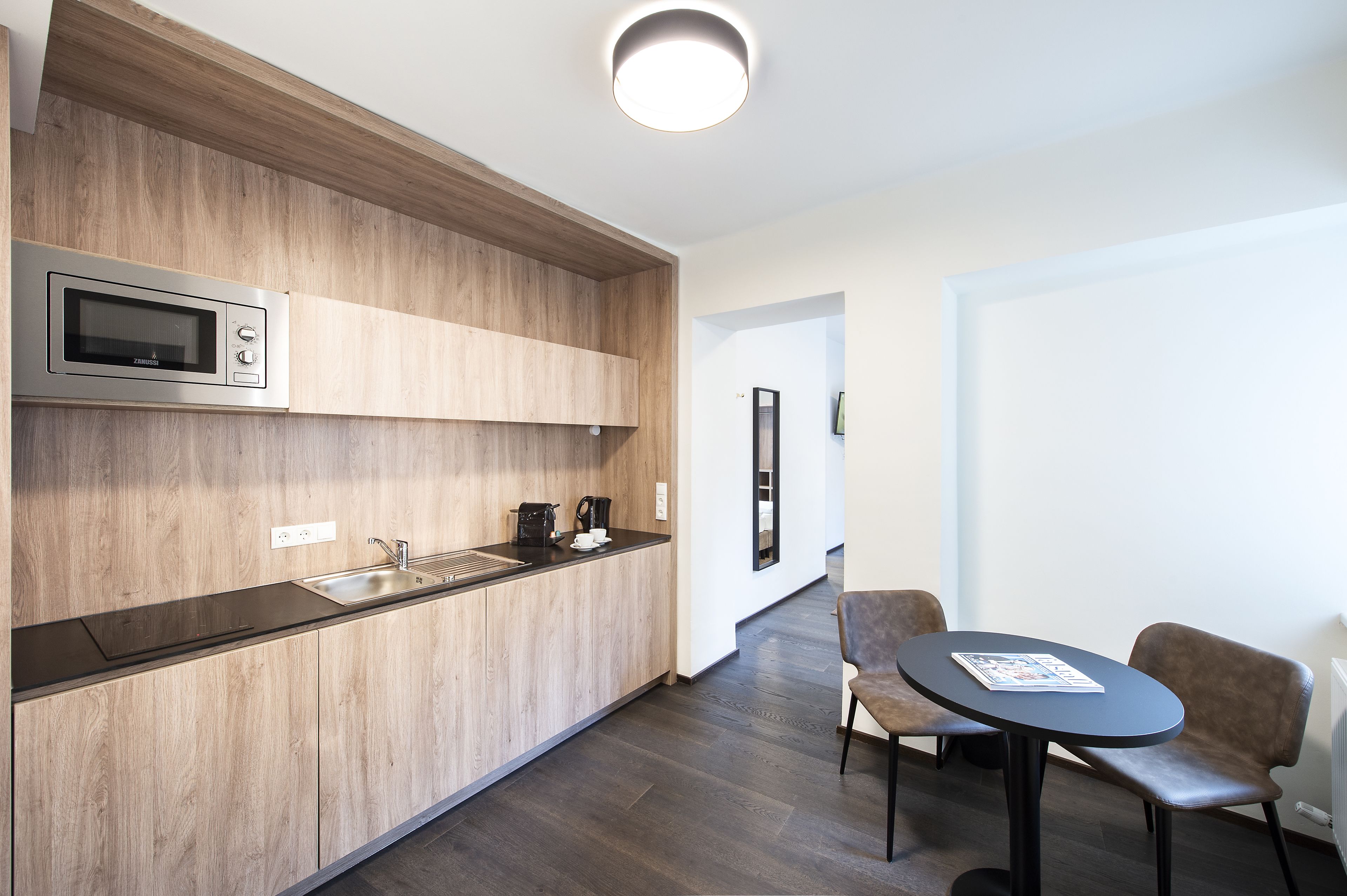 A modern kitchen with a built-in microwave, a sink, and a coffee maker. There is a dining area with a table and chairs.