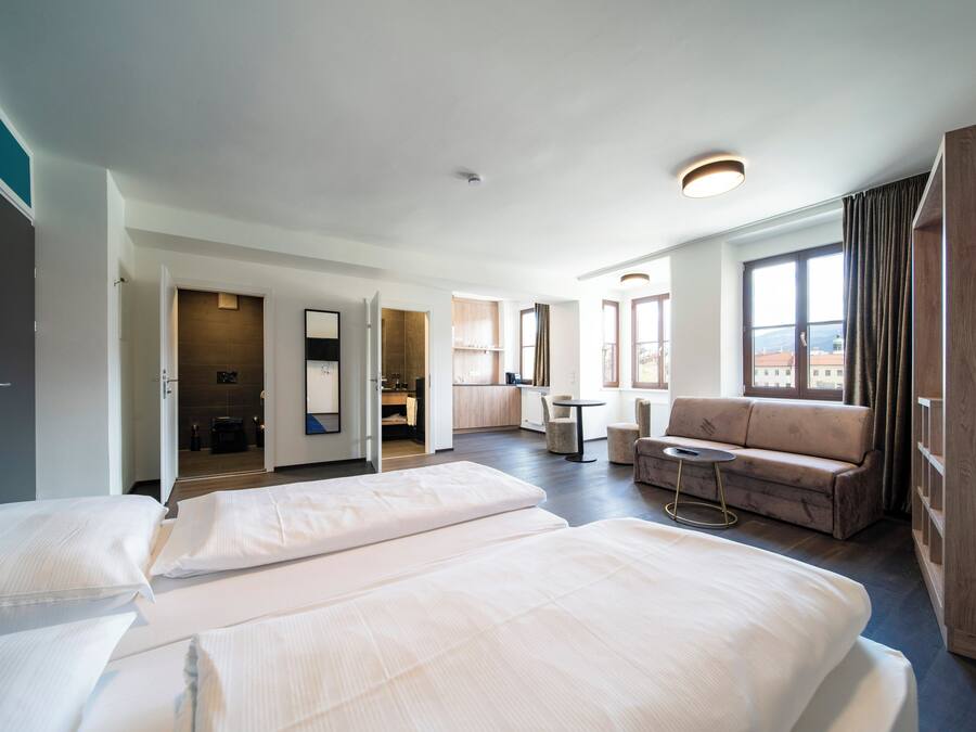 Ett hotellrum med två sängar, en soffa, ett litet bord och utsikt över staden.