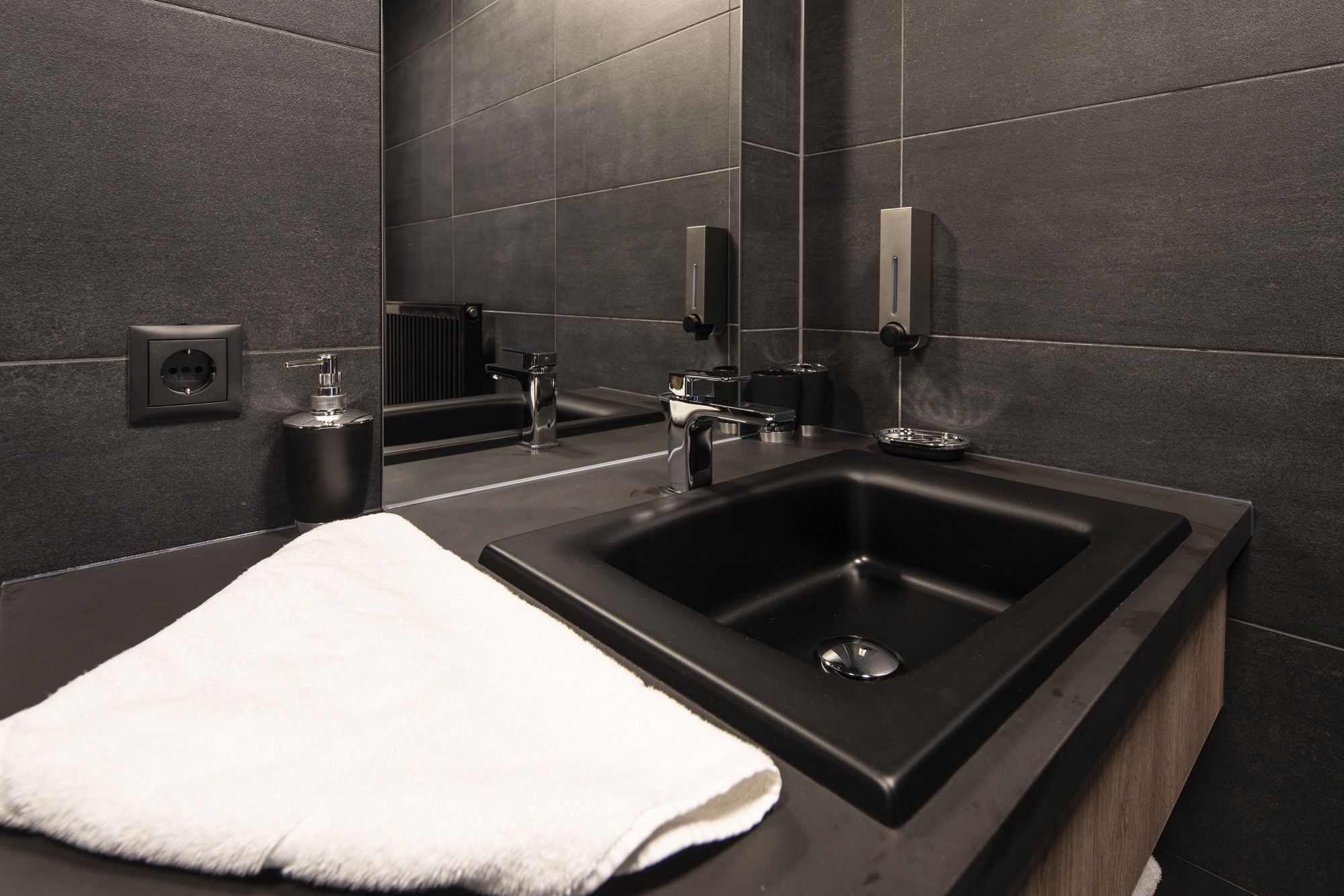 A modern bathroom with a black sink, a mirror, and a towel on the counter.
