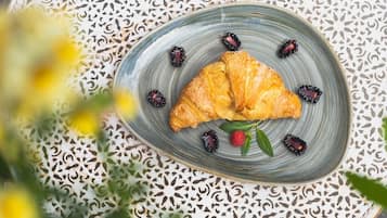 A plate with a croissant and berries on a patterned tablecloth.