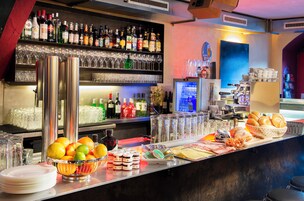 Zona de bar con estantes llenos de botellas de licor, vasos y un frutero.