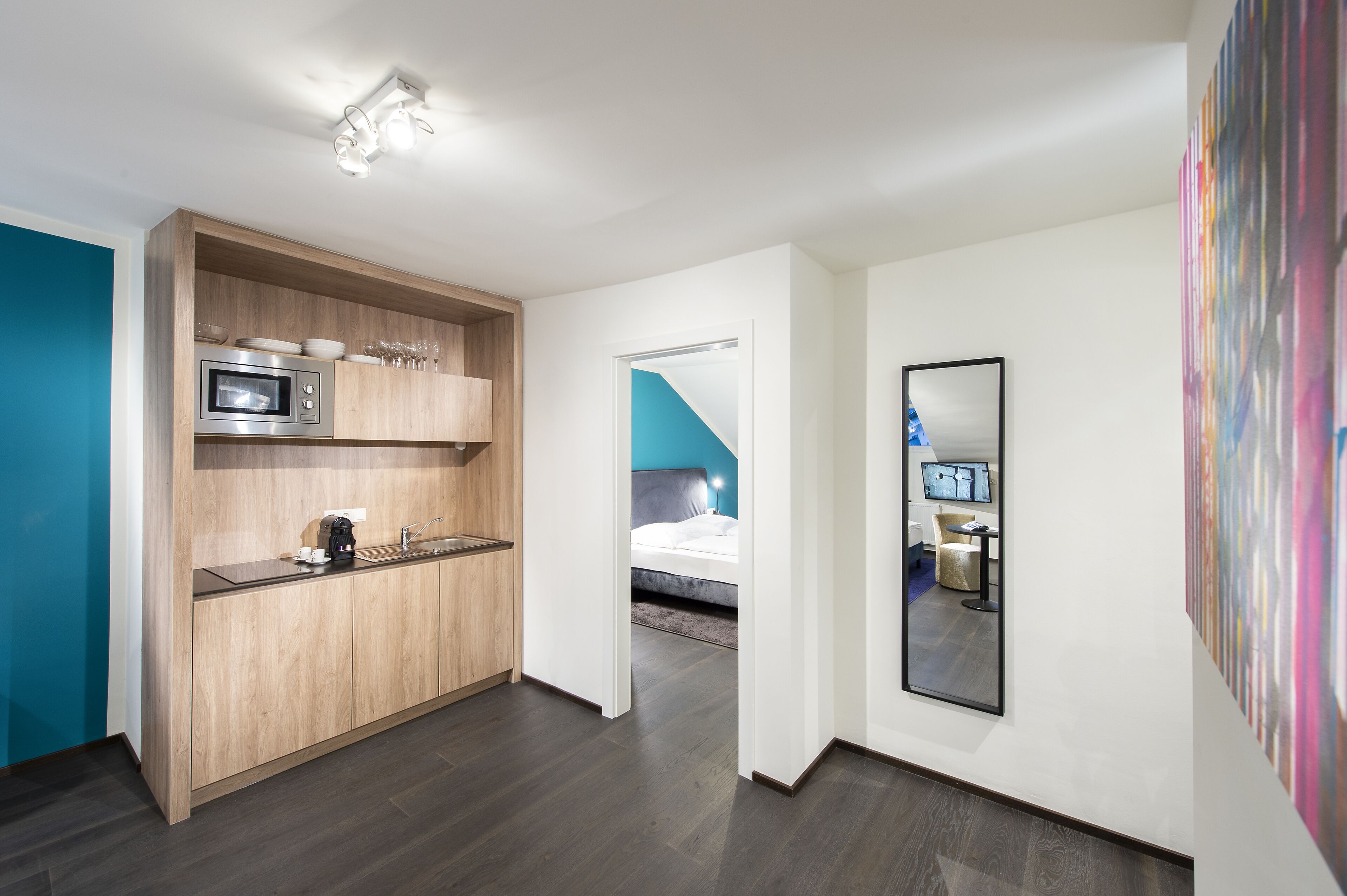 A modern hotel room with a kitchenette, a bed, and a large mirror.
