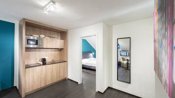 A modern hotel room with a kitchenette, a bed, and a large mirror.