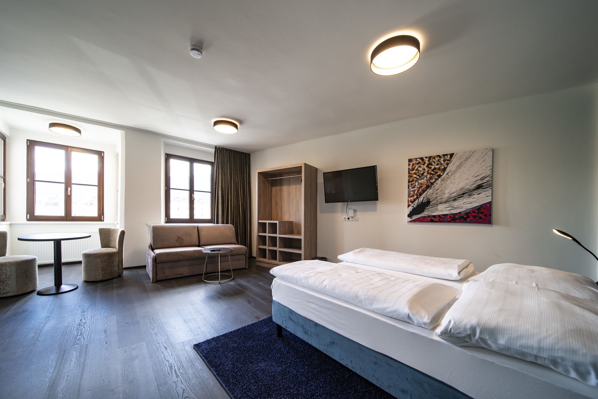 A modern hotel room with a bed, a sofa, a small table, and a TV.