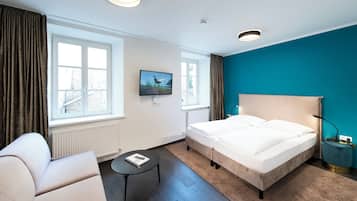 Ein Hotelzimmer mit Bett, Schreibtisch, Stuhl, Fernseher und einem Fenster mit Vorhängen.