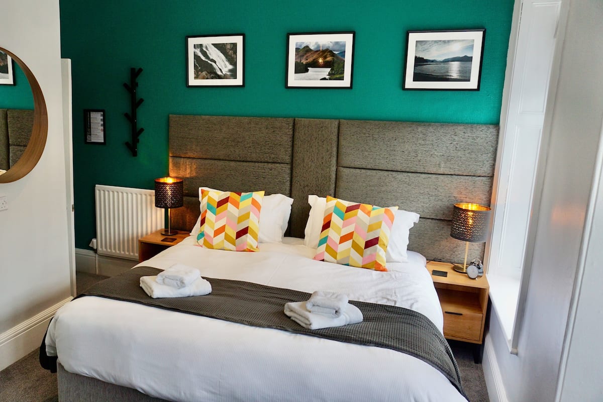Hotelkamer met een groot bed, twee nachtkastjes met lampen, een ronde spiegel en drie ingelijste foto's aan de muur.