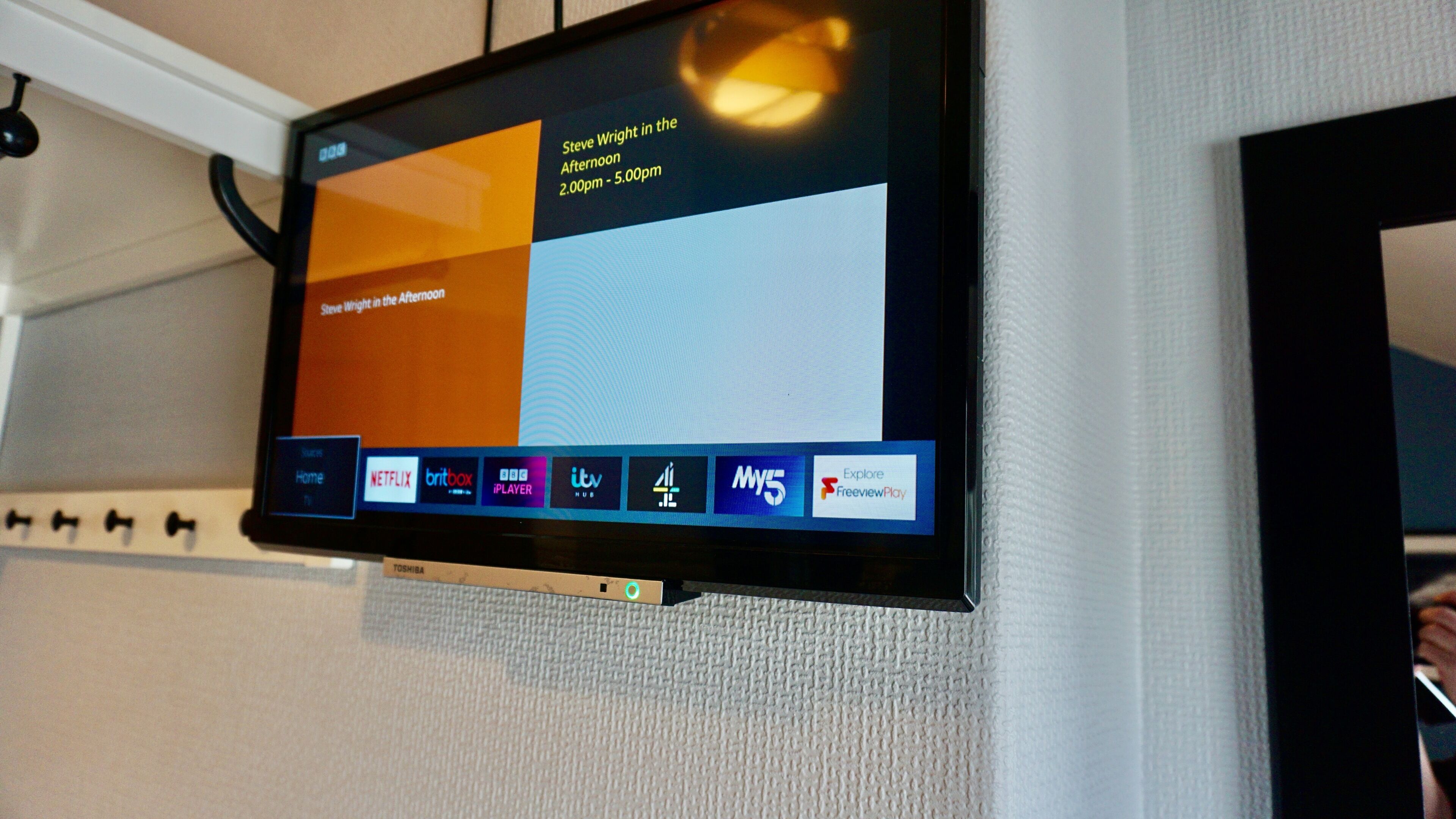 A flat-screen TV mounted on a wall displaying a TV guide with various channels and programs.