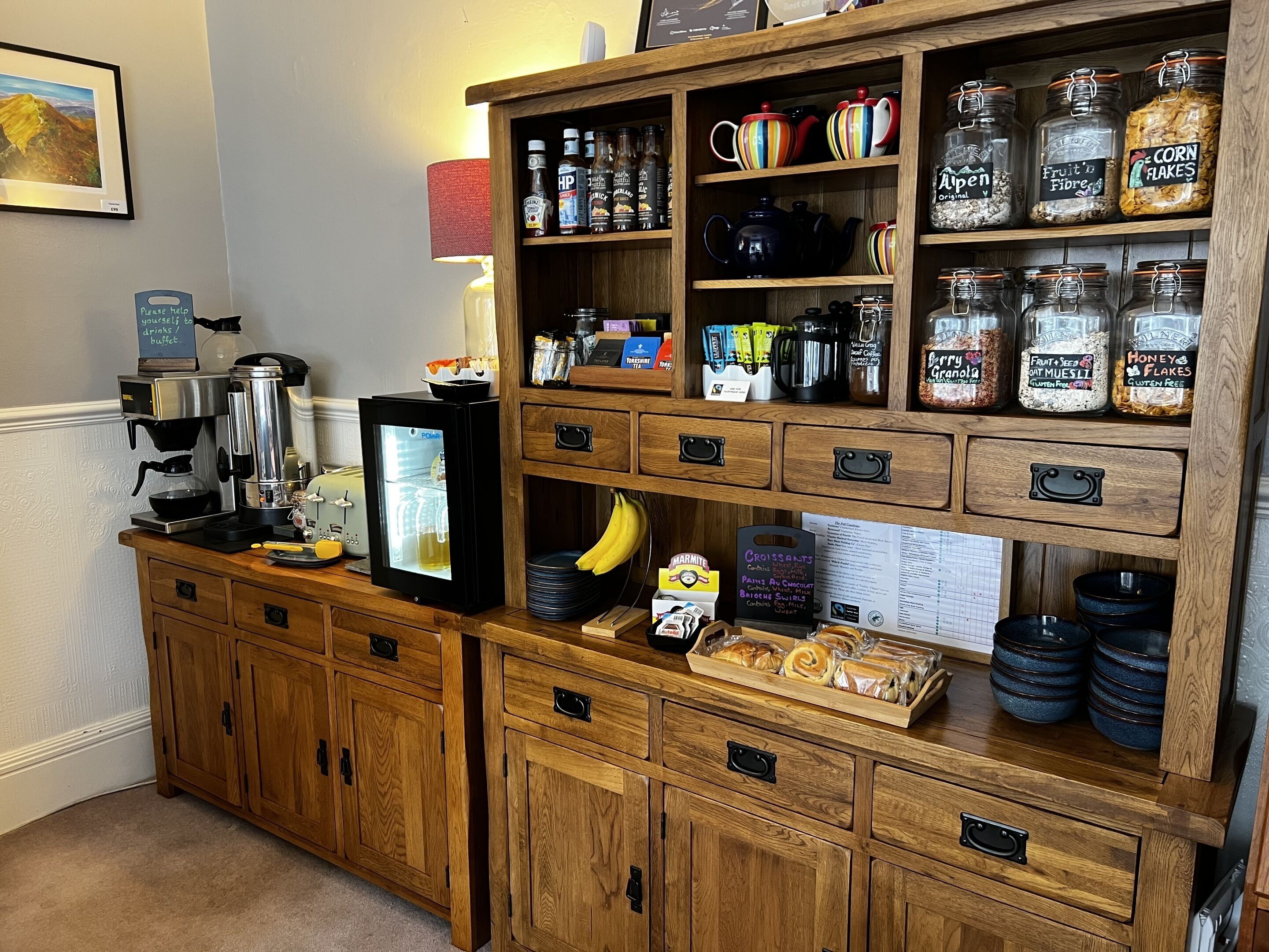 A kitchenette with a coffee machine, a refrigerator, and various food items on shelves.