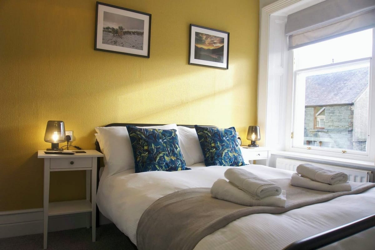 Een slaapkamer met een bed, twee nachtkastjes, een raam en twee foto's in lijsten aan de muur.