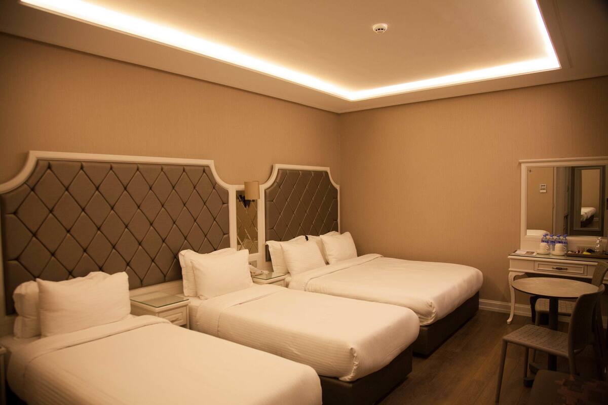A hotel room with three beds, a desk, a chair, and a mirror.