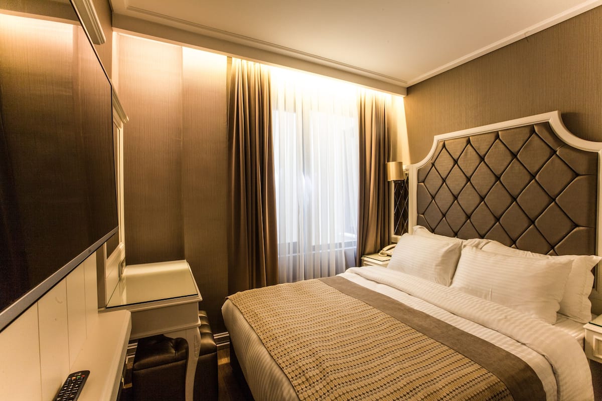 A hotel room with a bed, bedside table, lamp, and a TV.