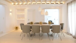 Un comedor moderno con una mesa larga, seis sillas, lámparas colgantes y vistas a la cocina.