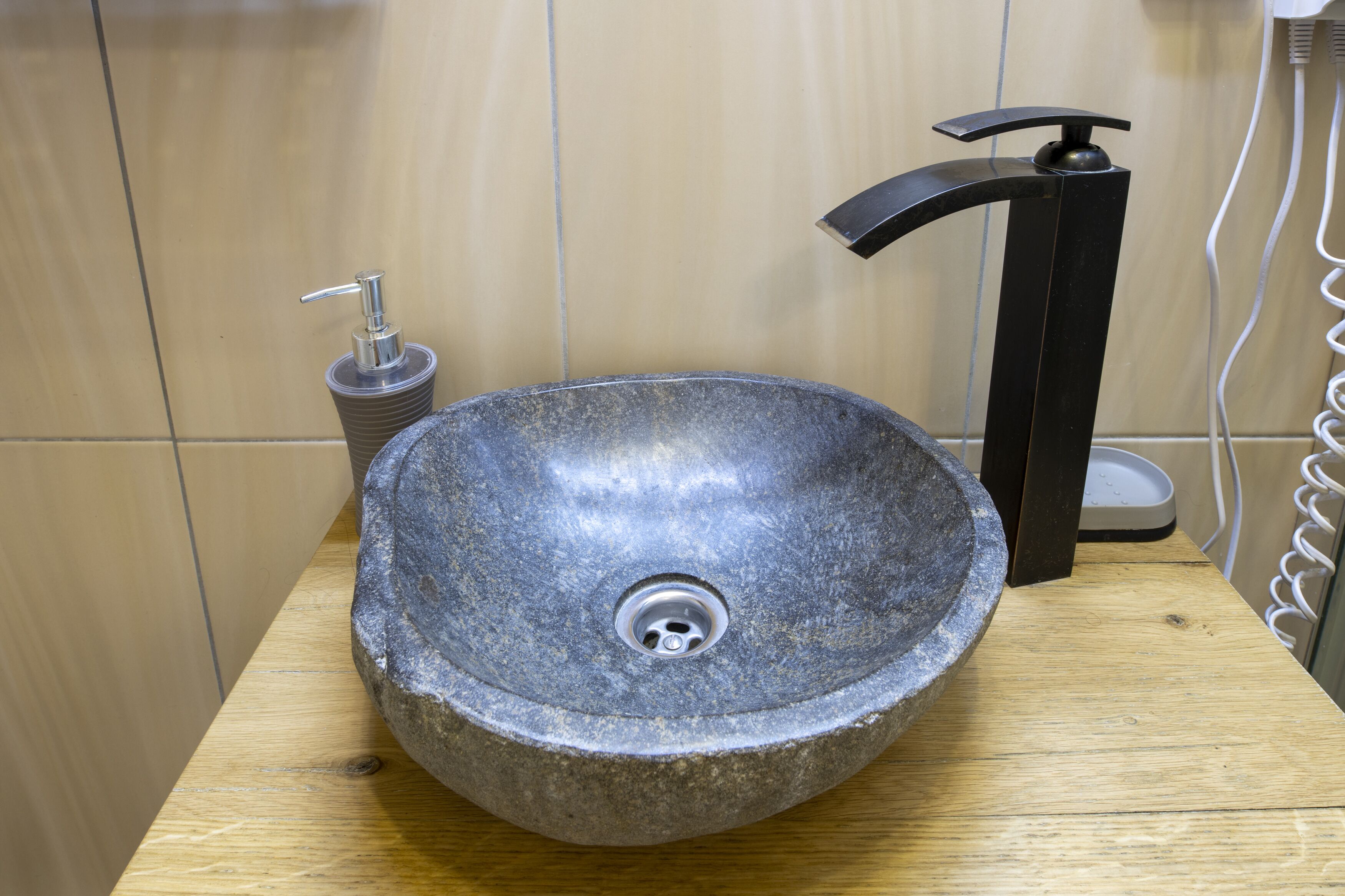 A stone sink with a modern faucet and a soap dispenser on a wooden countertop.