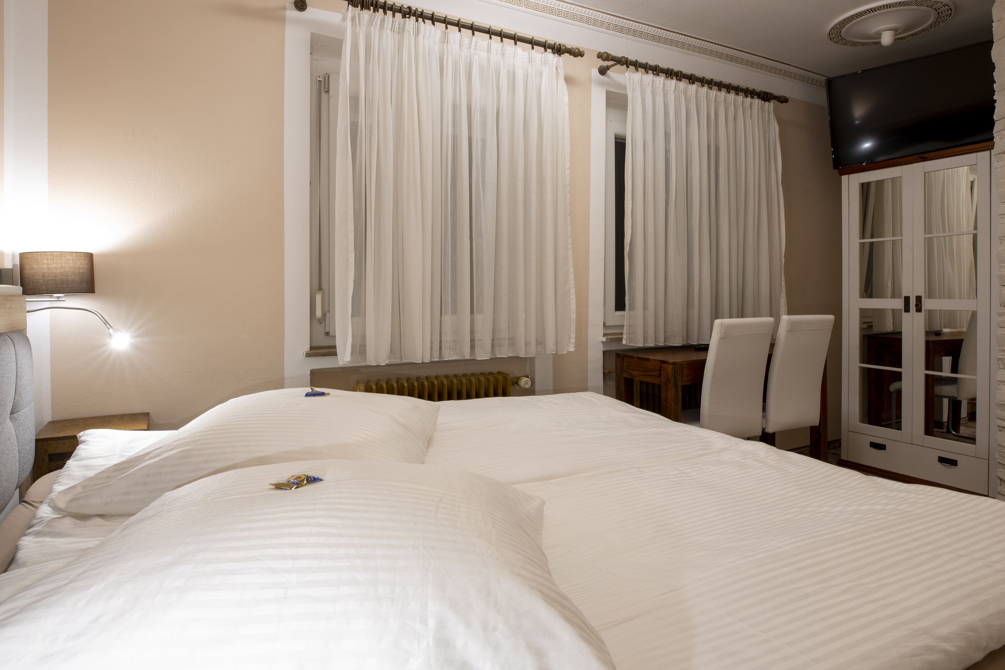 Hotellihuone, jossa on suuri sänky, työpöytä, kaksi tuolia, patteri ja vaatekaappi.