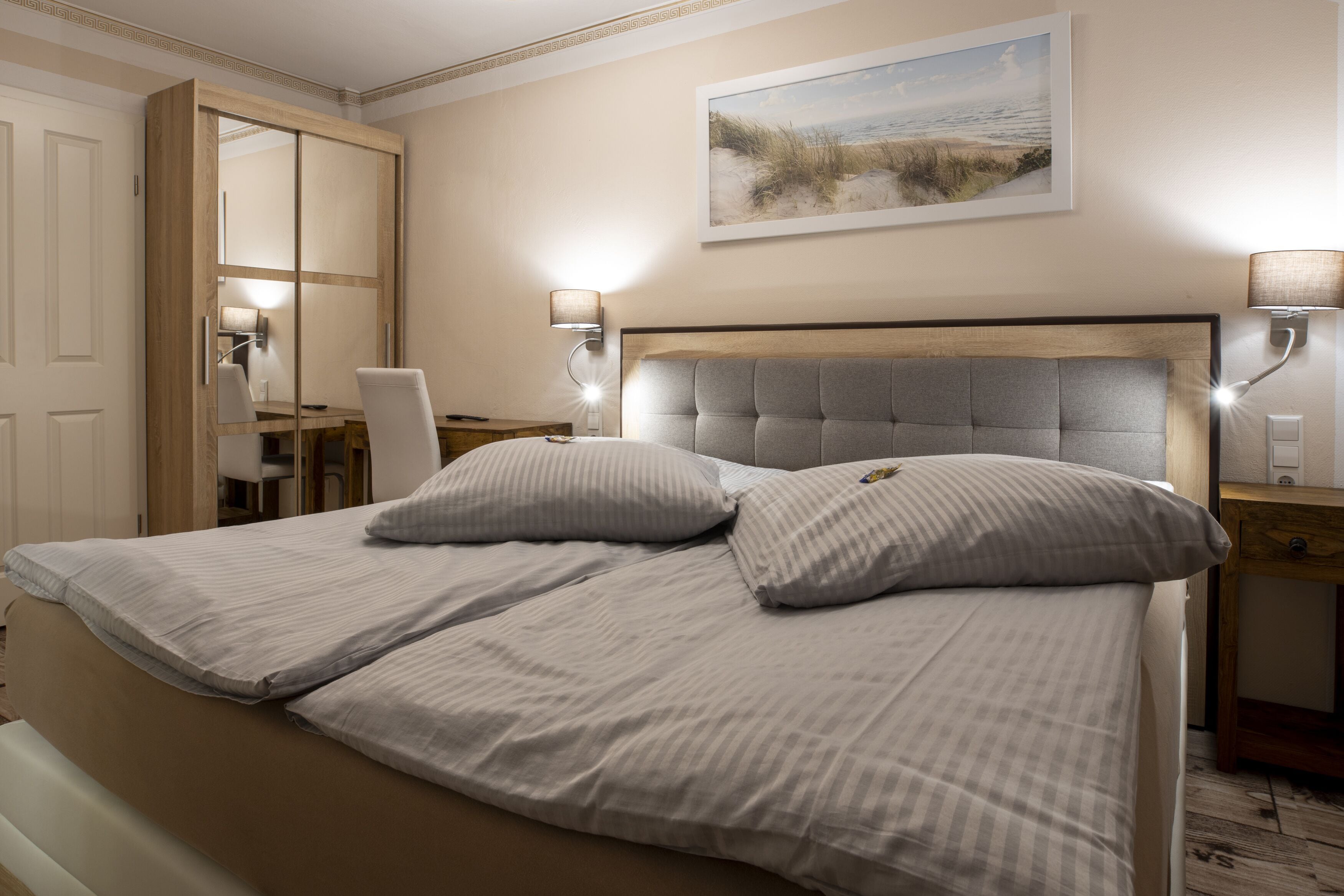 Un dormitorio con una cama grande, un escritorio y una silla. Hay un cuadro en la pared y una lámpara sobre el escritorio.