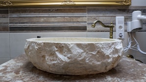 A stone sink with a gold faucet in a bathroom with marble walls and a gold-framed mirror. - Hotel Restaurant Meteora (Tuebingen)