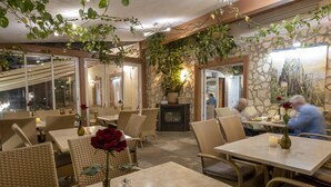 An indoor dining area with wicker furniture, tables, and chairs, featuring a stone wall and a fireplace. - Hotel Restaurant Meteora (Tuebingen)