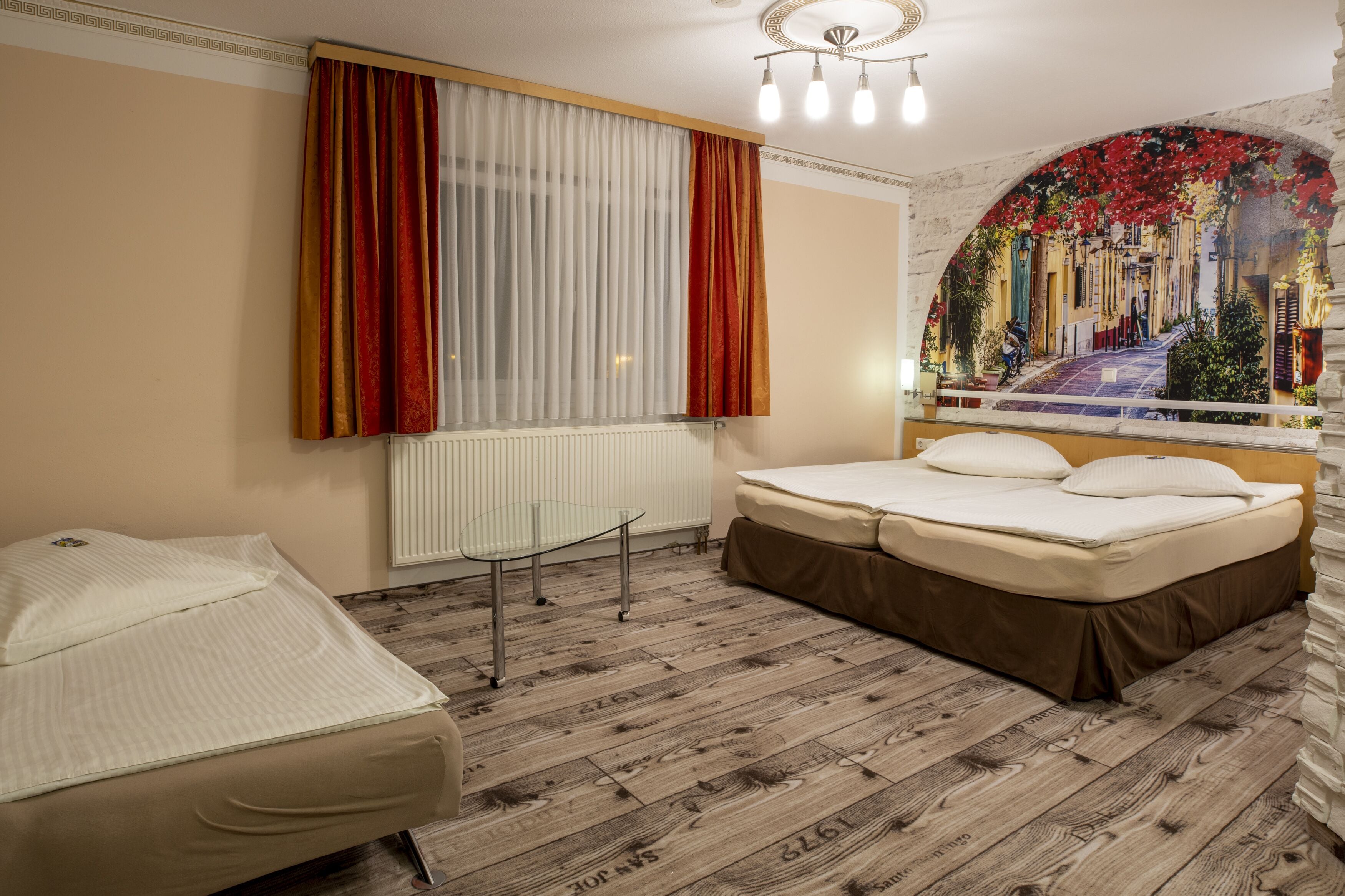 A hotel room with a bed, a small table, and a window with curtains.