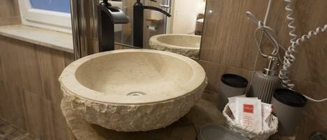 Une salle de bain avec un lavabo en pierre, un miroir, un porte-serviettes et un panier contenant des articles de toilette.
