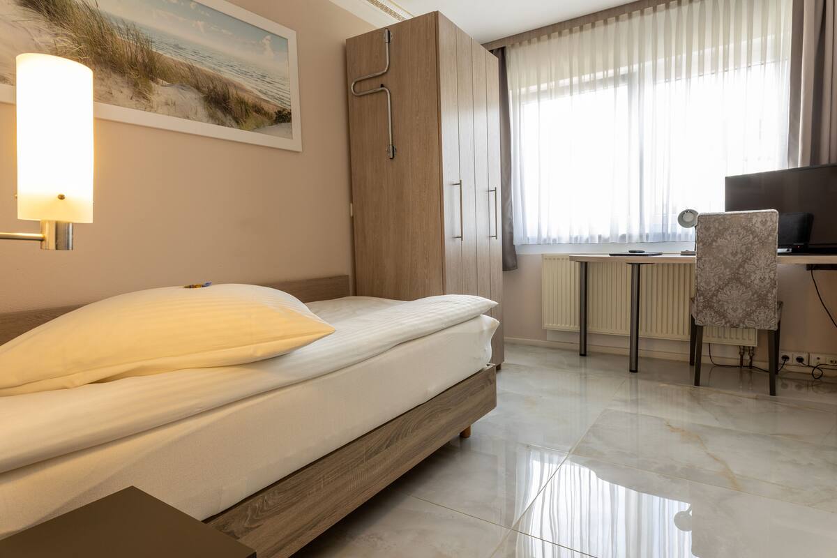 A bedroom with a bed, a desk, a chair, and a TV.