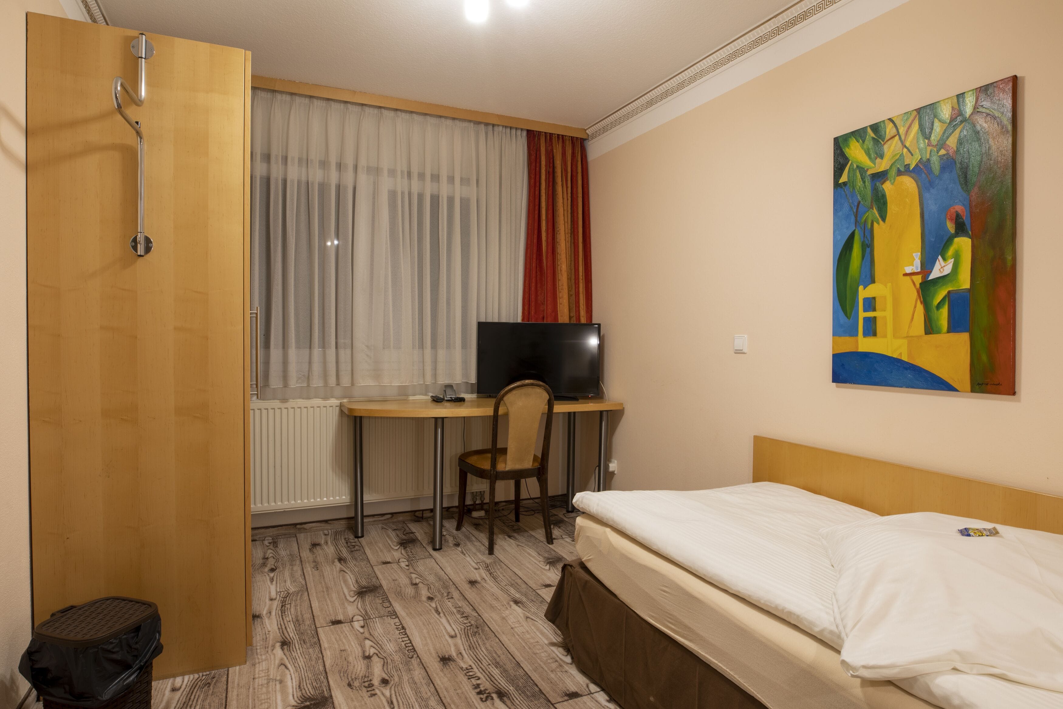Ein Hotelzimmer mit einem Holztisch, einem Fernseher, einem Bett und einem Bild an der Wand.