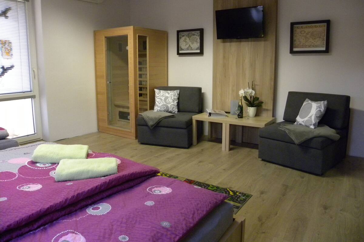 A modern bedroom with a bed, two armchairs, a small table, and a TV.