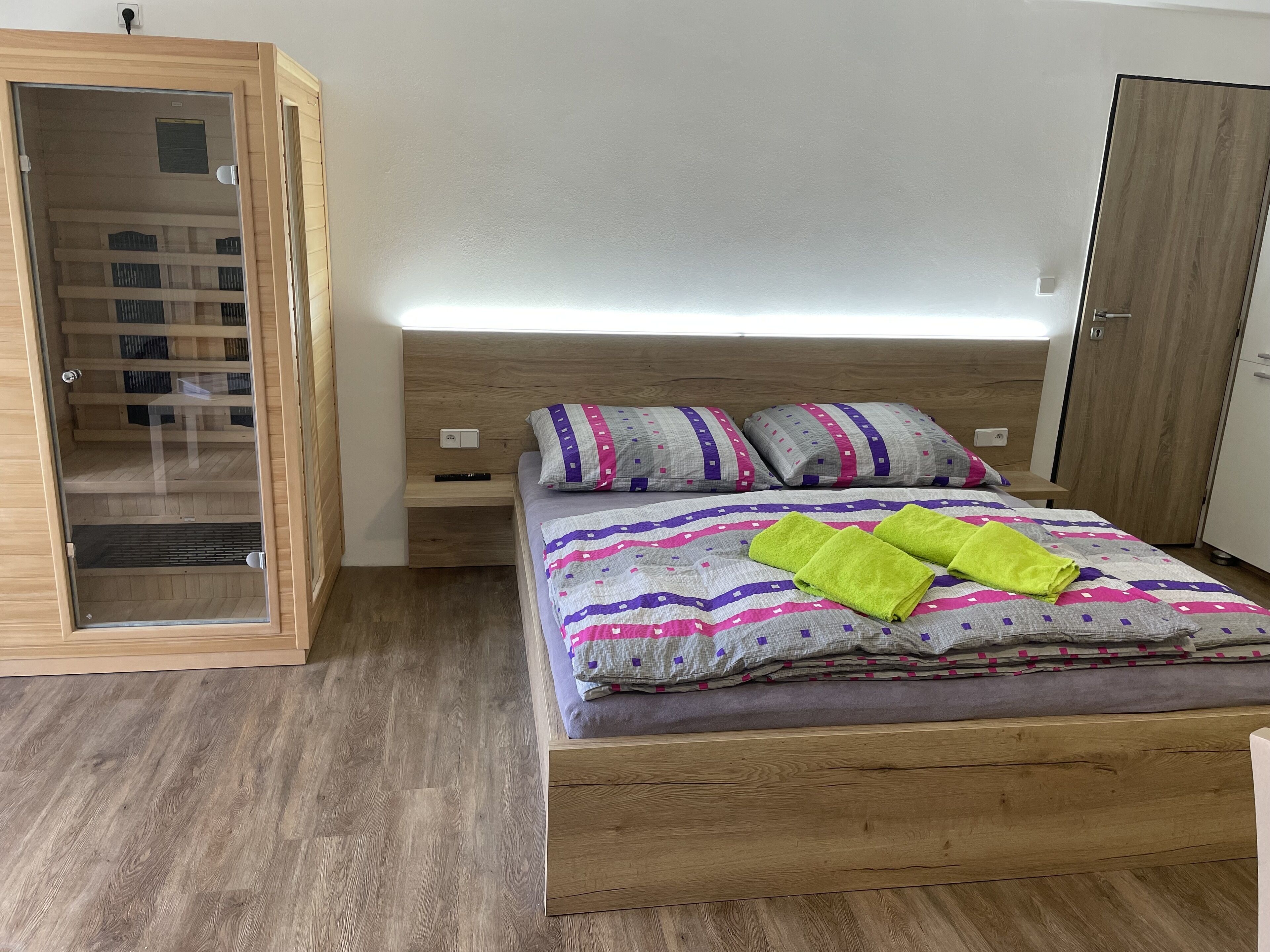 A bedroom with a wooden bed, a nightstand, a wardrobe, and a glass door leading to a storage area.