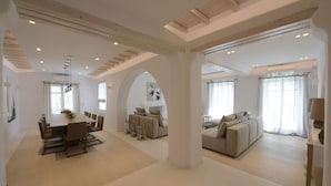 A spacious living area with a dining table, sofas, and a large window. - Villa Opal (Mykonos)