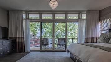 A bedroom with a large bed, a TV, a chandelier, and a sliding glass door leading to an outdoor seating area.