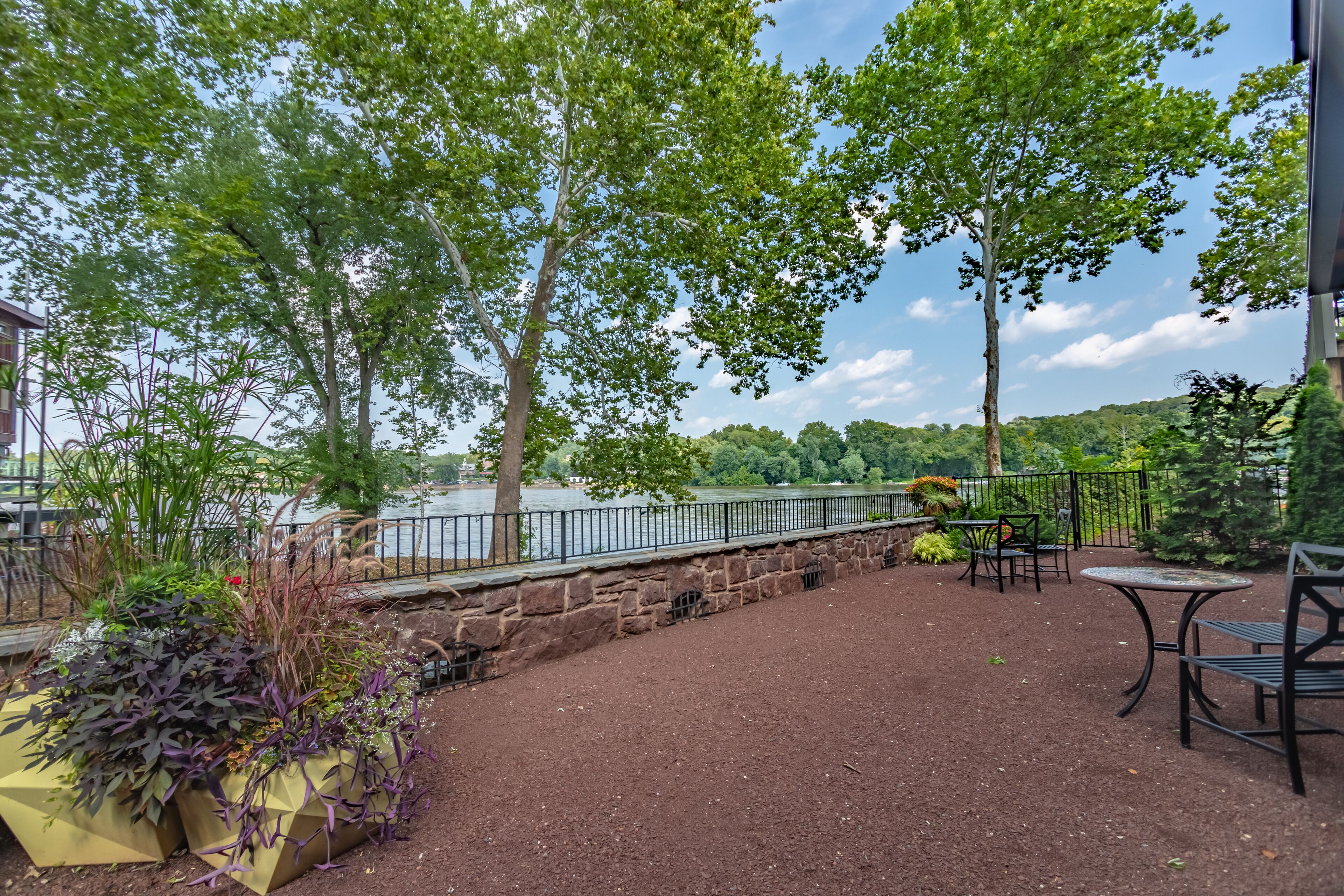 An outdoor patio with stone walls, tables, and chairs overlooking a body of water.