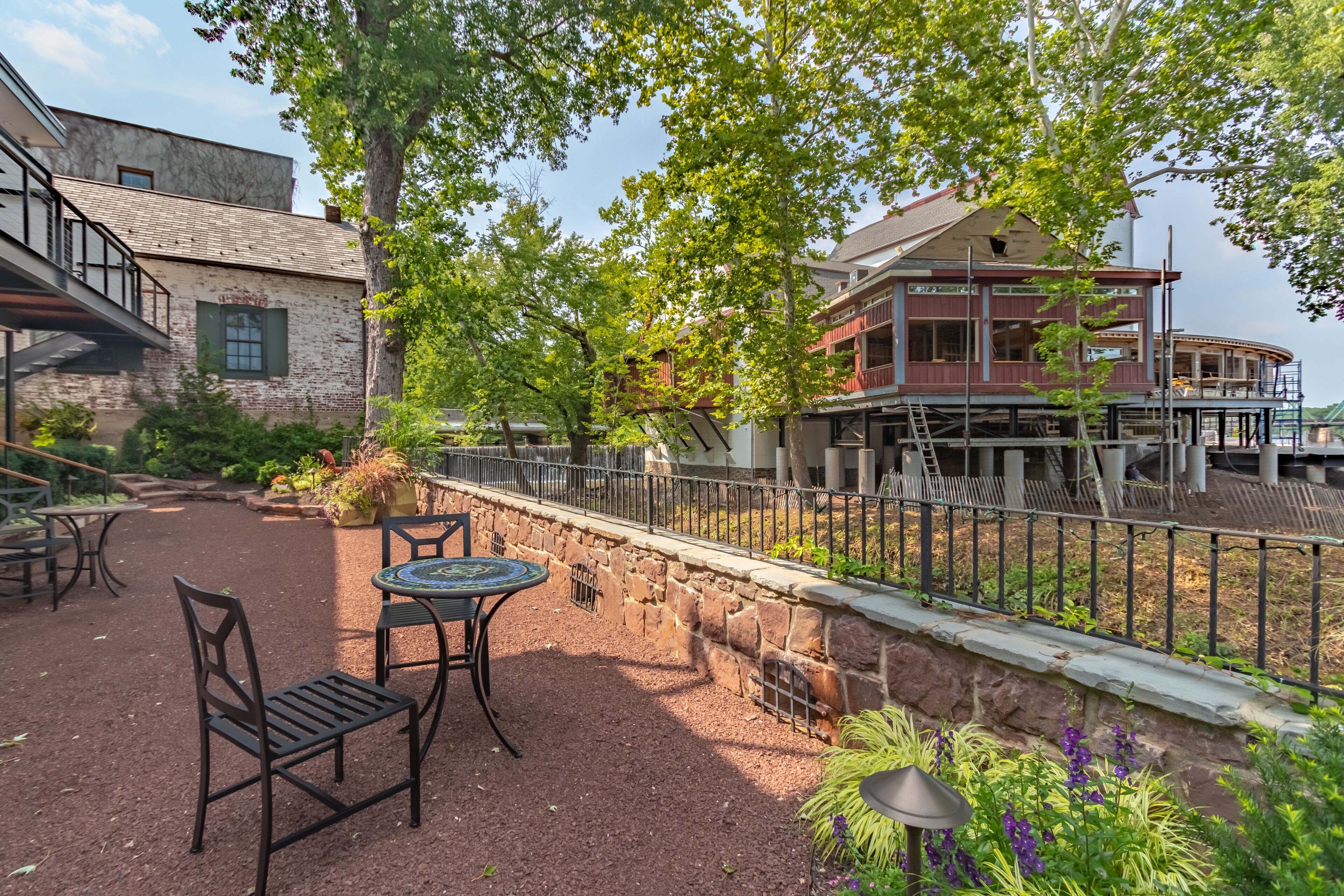 An outdoor patio with tables and chairs, a stone wall, and a wooden deck with railings.