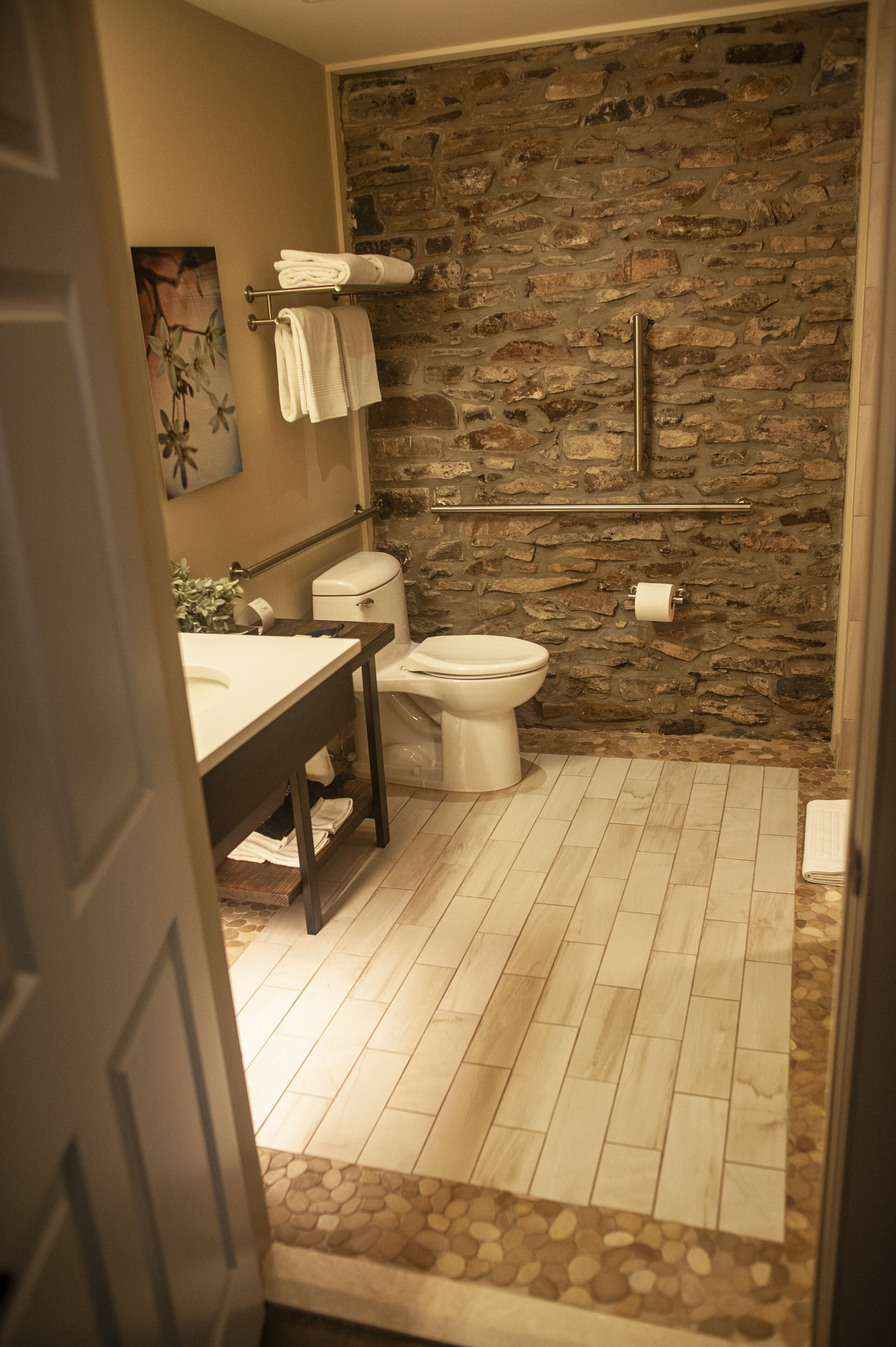 A bathroom with a stone wall, a toilet, a sink, and a towel rack.