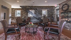 A spacious lobby with a stone wall, a staircase, and leather chairs around a central table with flowers. - Carriage House of New Hope (New Hope)