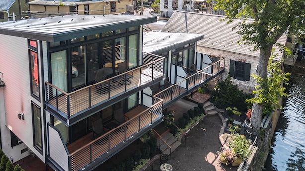 A modern multi-story building with a glass facade, a balcony with outdoor seating, and a view of a river. - Carriage House of New Hope (New Hope)