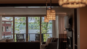 A room with a large window overlooking a river and a bridge, furnished with a sofa and chairs, and a hanging light fixture. - Carriage House of New Hope (New Hope)
