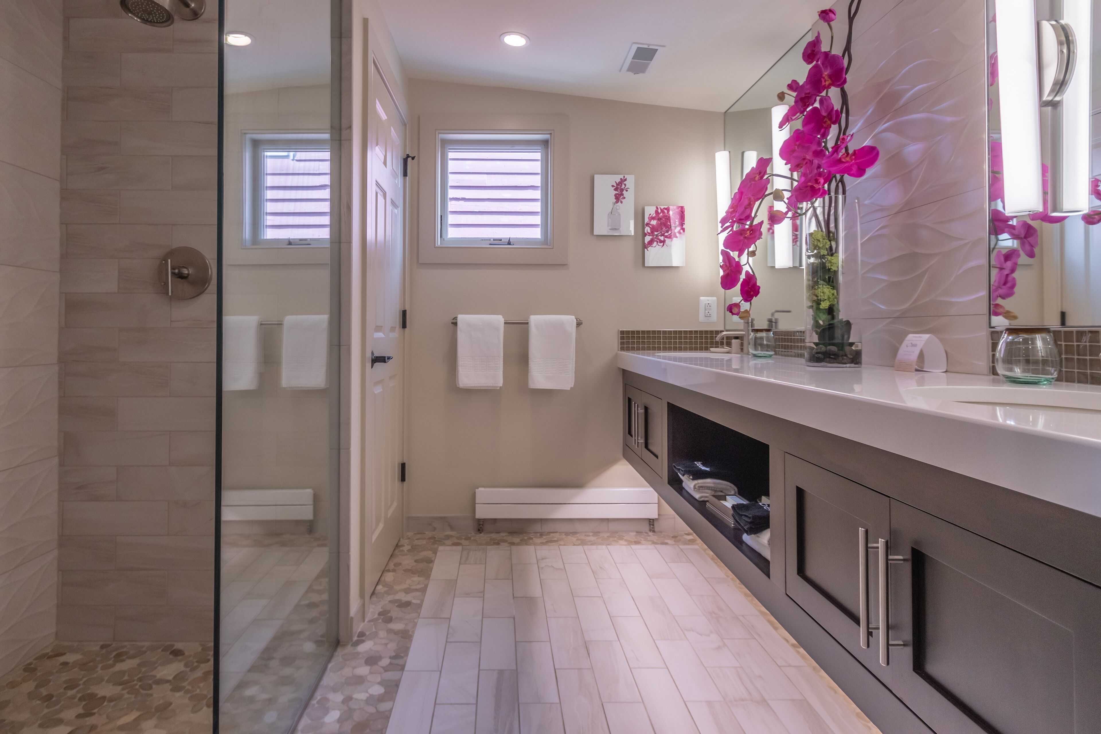 A modern bathroom with a glass shower enclosure, a vanity with a mirror, and a bench.