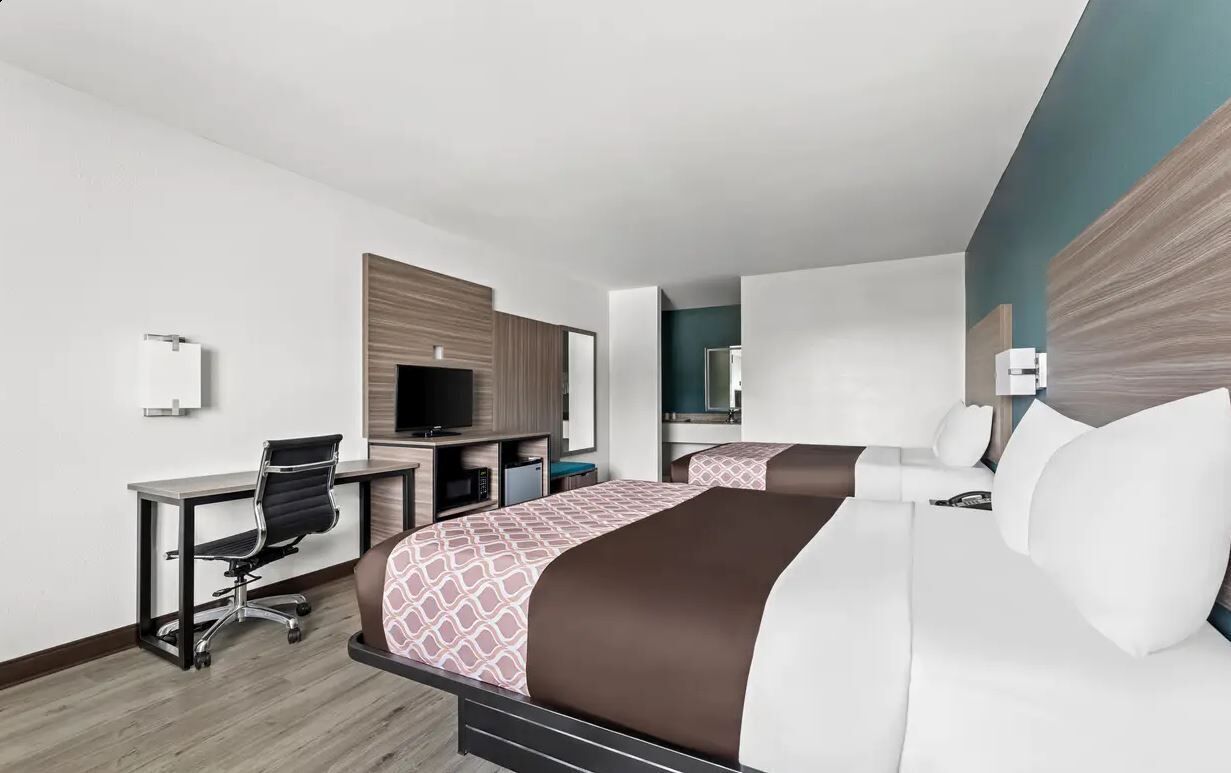 Habitación de hotel con dos camas, un escritorio, una silla, un televisor y un espejo.