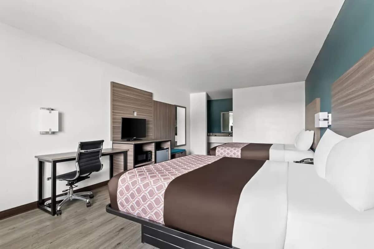 Habitación de hotel con dos camas, un escritorio, una silla, un televisor y un espejo.