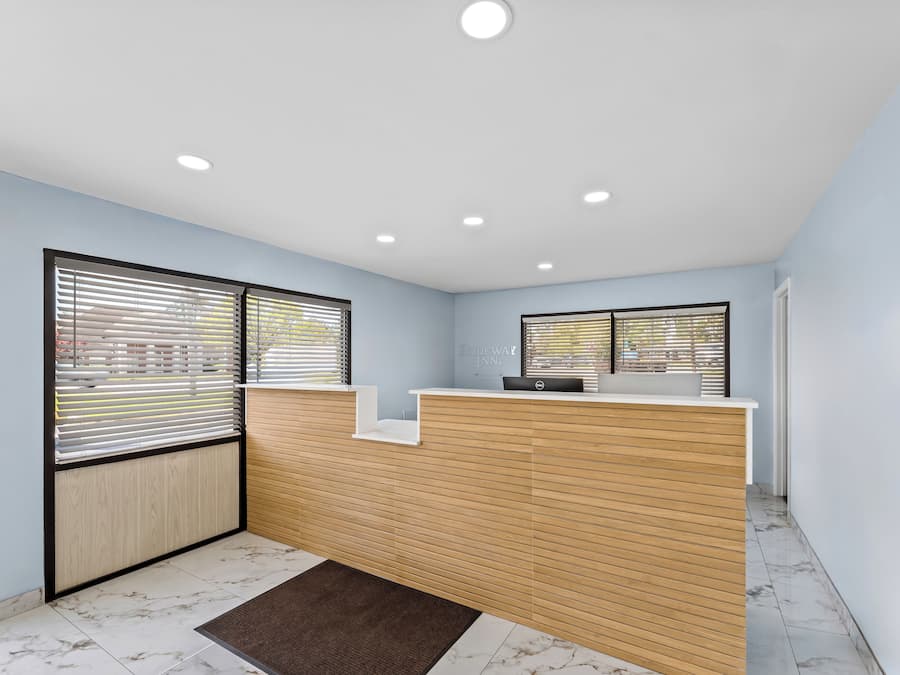 A reception desk with a wooden panel design, two windows with blinds, and a marble-tiled floor.