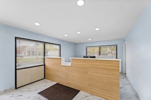 A reception desk with a wooden panel design, two windows with blinds, and a marble-tiled floor.